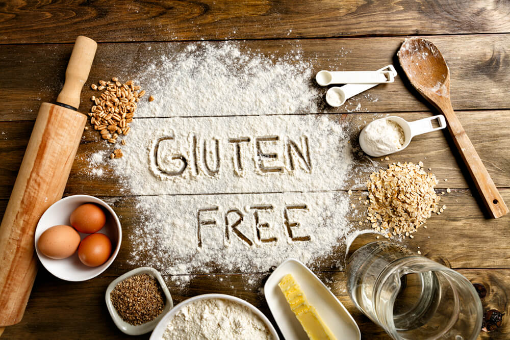Photo with the words gluten free written in flour. Rolling pin eggs, flour and butter are also featured.